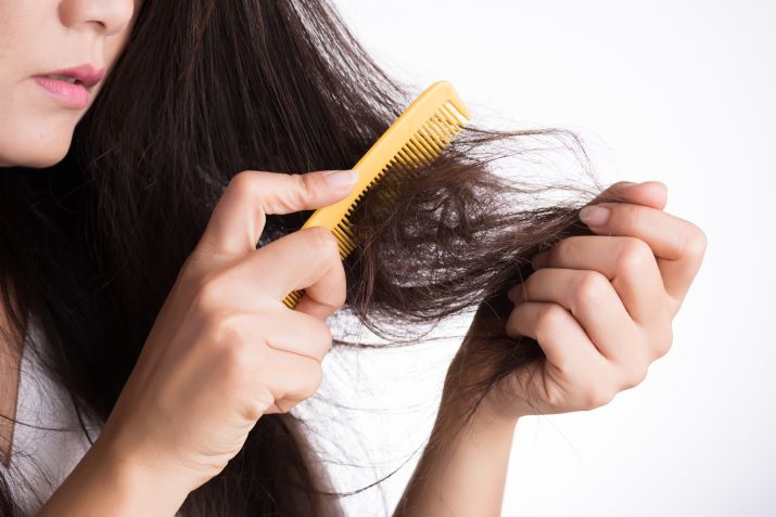 Woman combing her dry, damaged hair while looking at it.