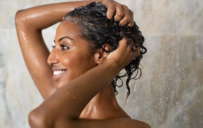 Smiling woman washing her hair in the shower at home.